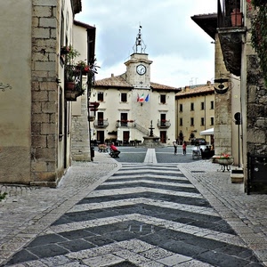 orologio, piazza, fontana, bandiere, strada, finestre, panchine, torre, case, fiori, balconi, vasi, persone, piante, campanile, via, porte, banderuola, campana, vicolo